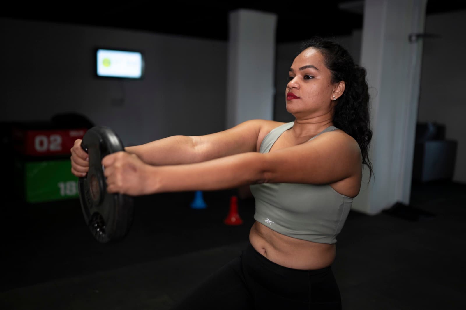 A FIT360 client performing a plate front raise in dramatic lighting